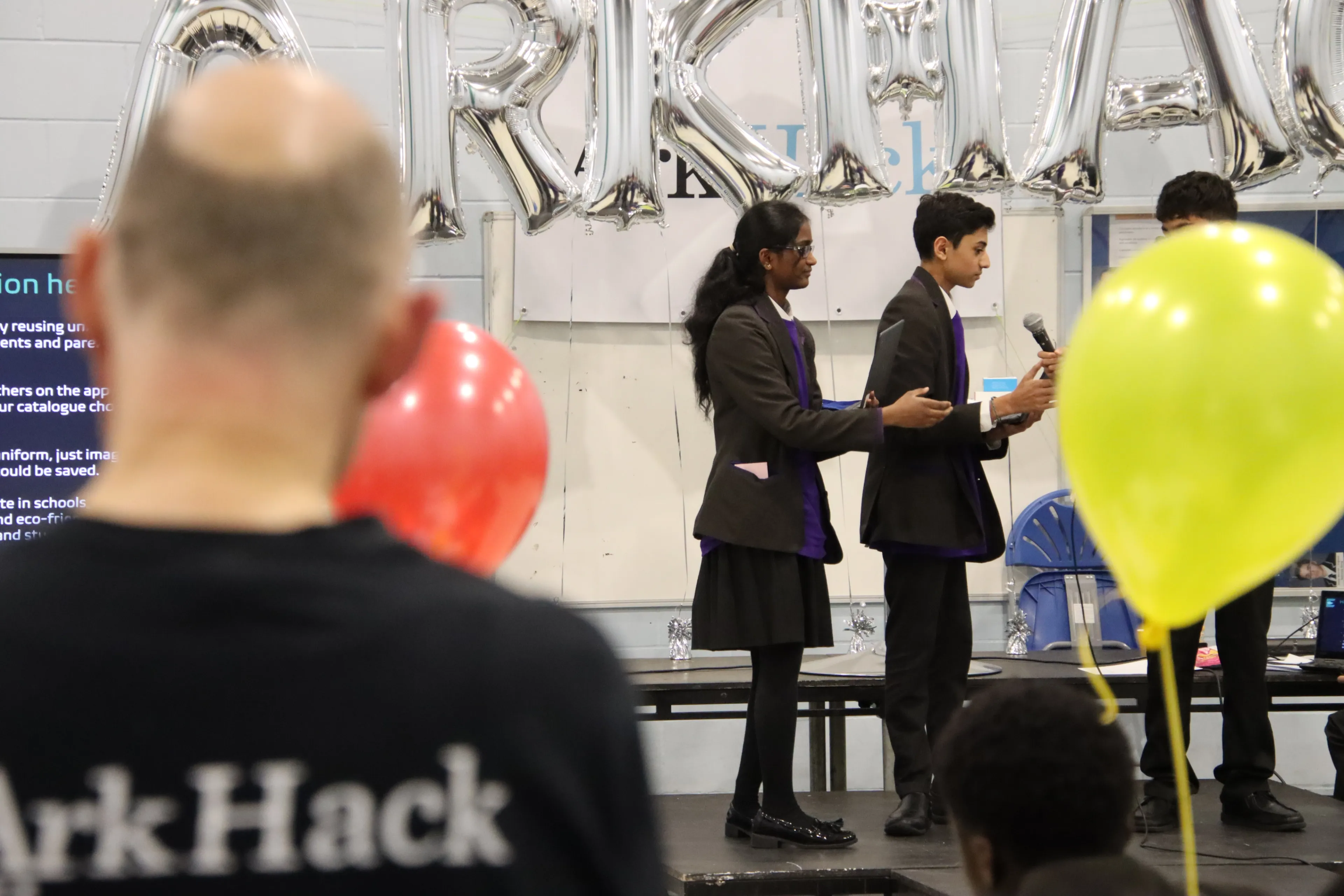 Pupils standing in front of a microphone. One is speaking and delivering their Arkhack pitch to an unseen audience.