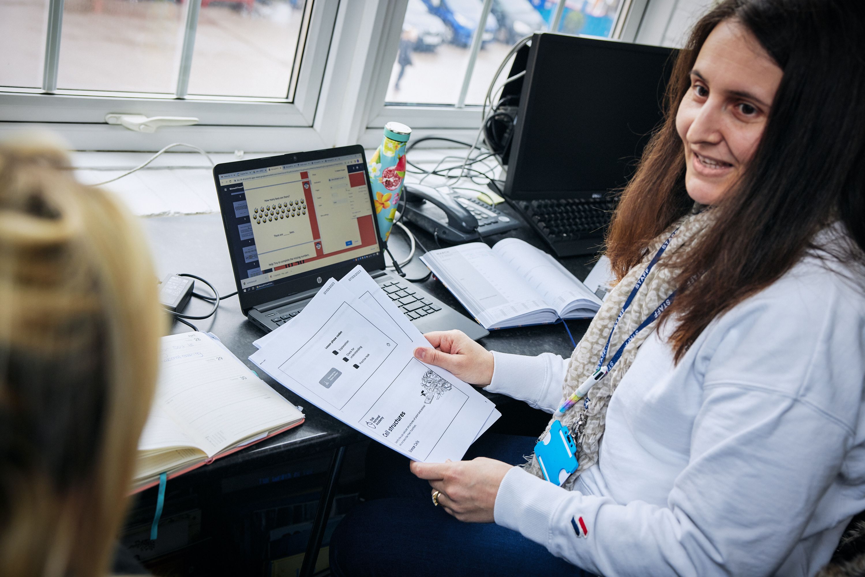 A teacher sat at a laptop holding printed resources