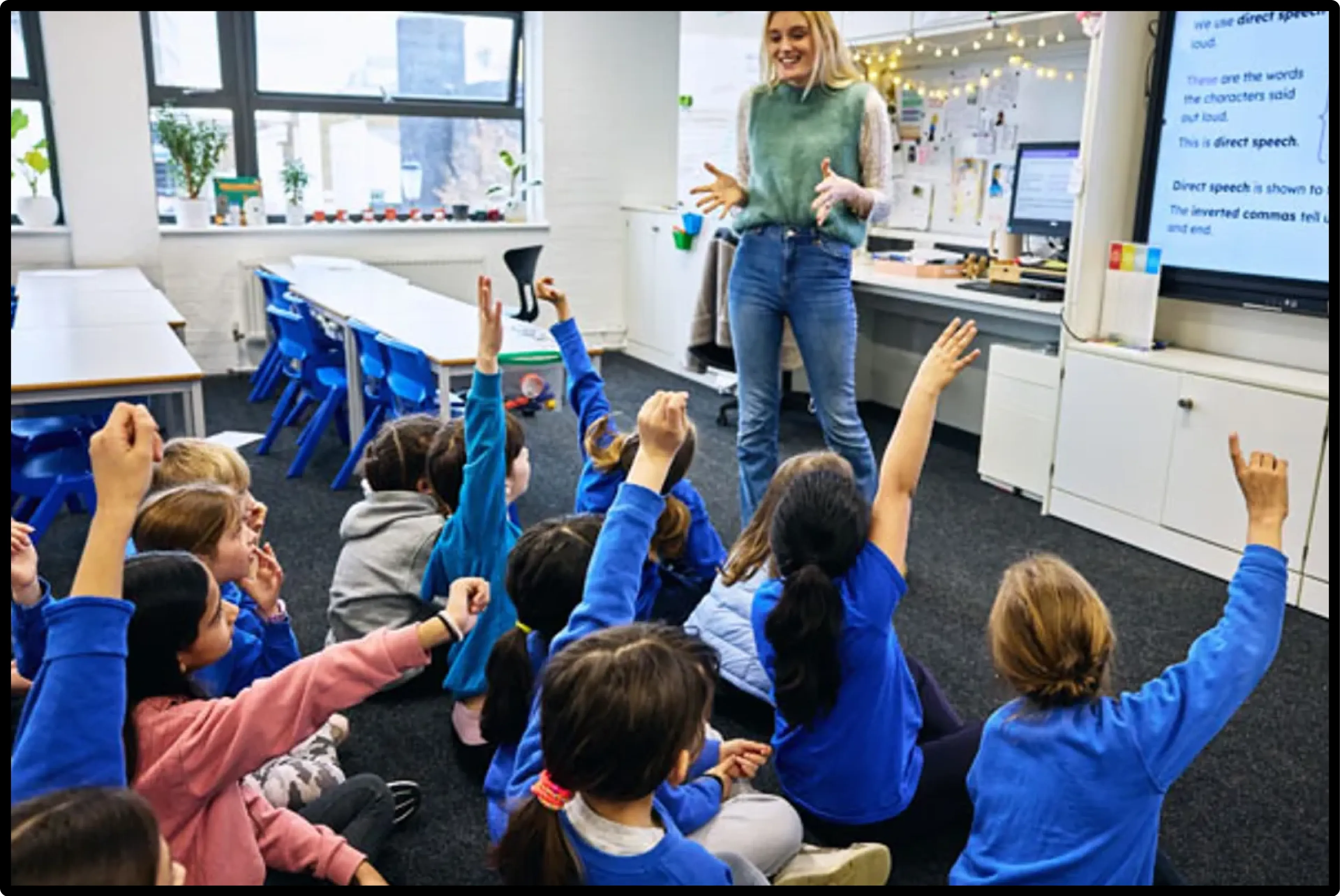 A teacher at the front of a classroom, delivering her lesson to her class of primary pupils.