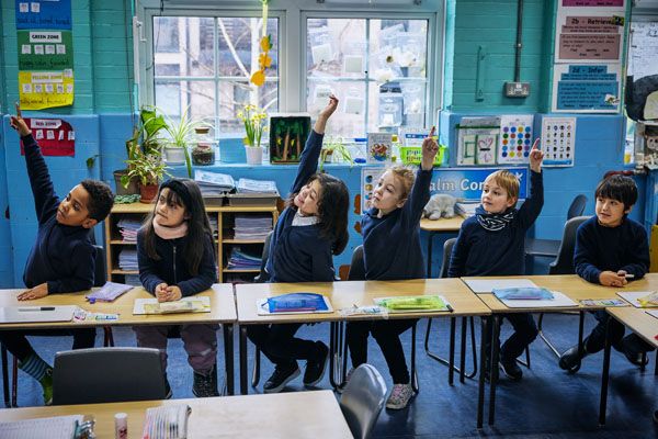 Primary school pupils in a lesson with their hands up to answer questions
