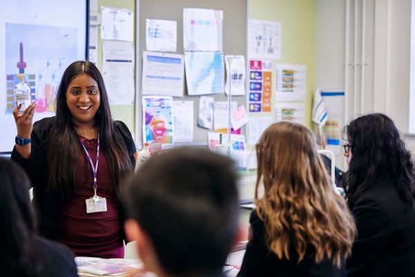 A science teacher holding a container of liquid stood at the front of a class of students 